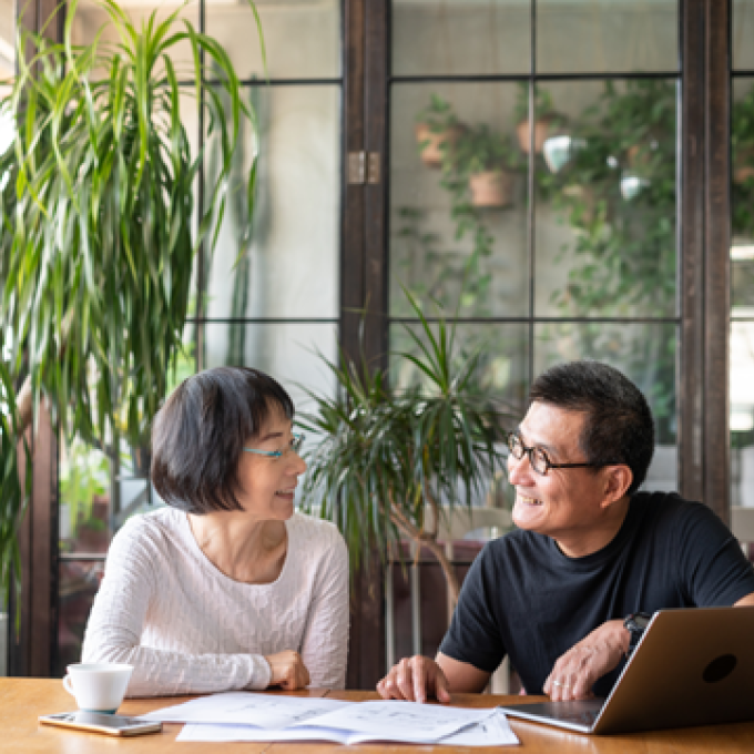 Two people smiling while working at a table with a laptop and papers.